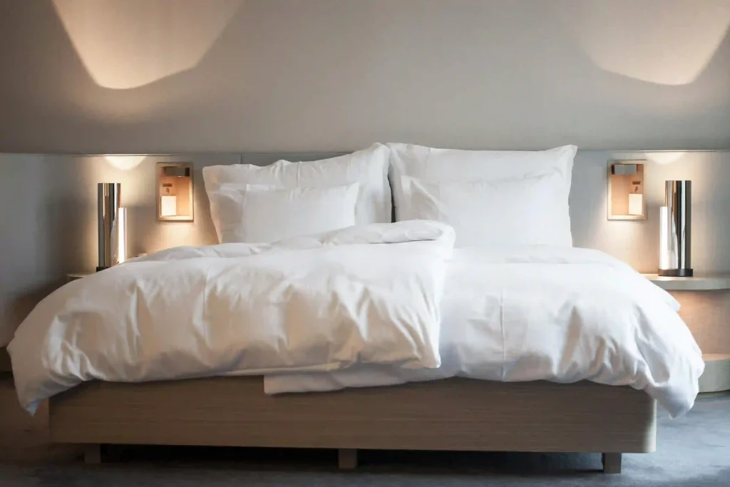 Hotel Zimmer Bett in weißen Lacken und zwei Nchttischlampen daneben.