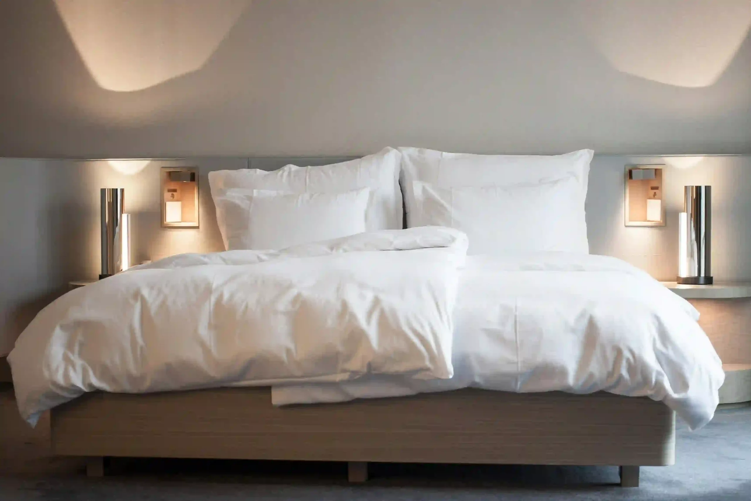 Hotel Zimmer Bett in weißen Lacken und zwei Nchttischlampen daneben.